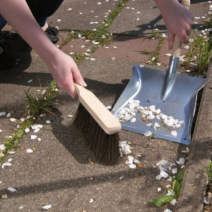 Een persoon veegt bloemblaadjes op een stoffer met een houten handveger.